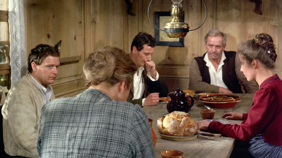 Drei Männer und zwei Frauen sitzen an einem Holztisch und essen "Znacht".