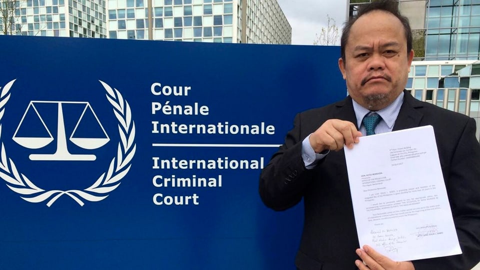 Ein Mann mit einem Schreiben in der Hand vor dem Schild des Internationalen Strafgerichtshofs.