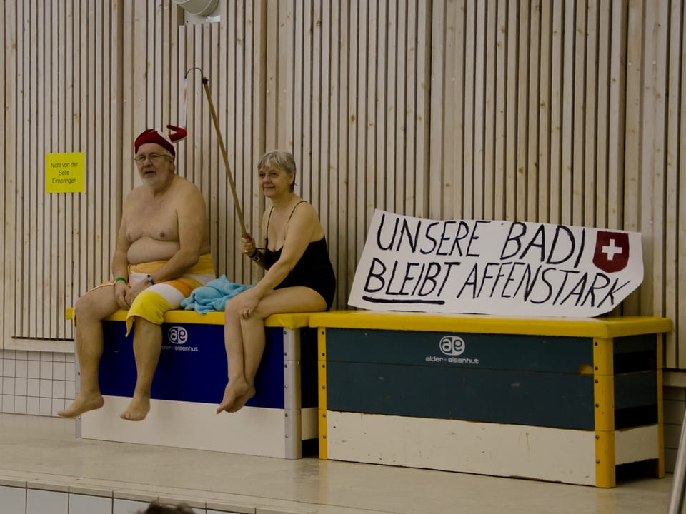 Zwei RheinauerInnen sitzen an der Demonstration für die Badi neben dem Beckenrand auf Schwedenkasten