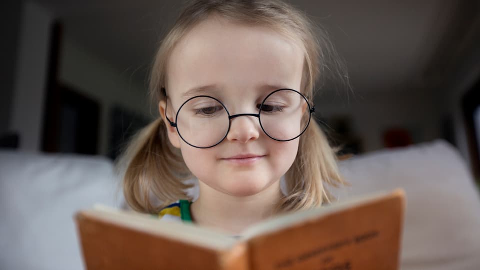 Kleines Mädchen mit Brille liest ein Buch.