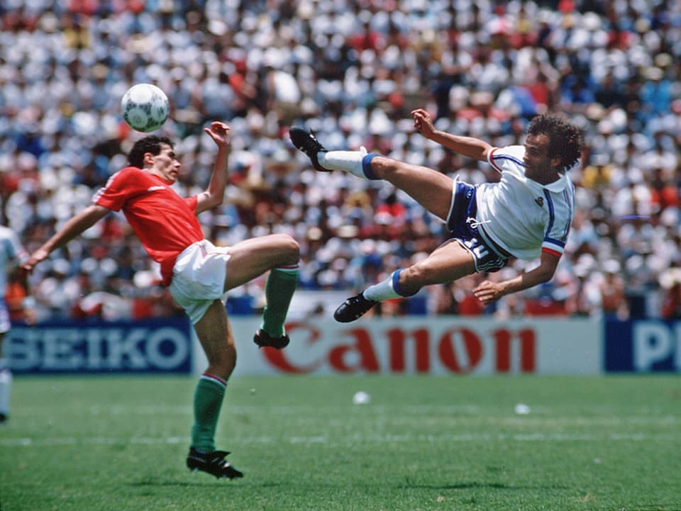 Spielszene aus der WM-Partie 1986 zwischen Ungarn und Frankreich. Michel Platini "hängt" bei eienm Seitfallzieher in der Luft.