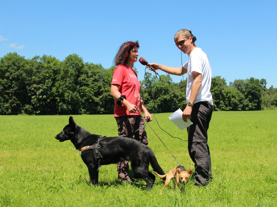 Frau und Reto Scherer mit zwei Hunden. Einem grossen schwarzen und einem kleinen braunen.