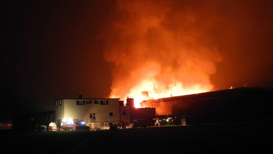 Feuer und Rauch über einem Gebäudekomplex, nachts.