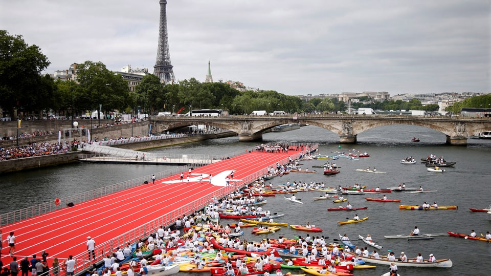 Blick auf die Seine von einer Brücke: Dutzende Kayaks bewegen sich rund um eine rot eingefärbte Plattform
