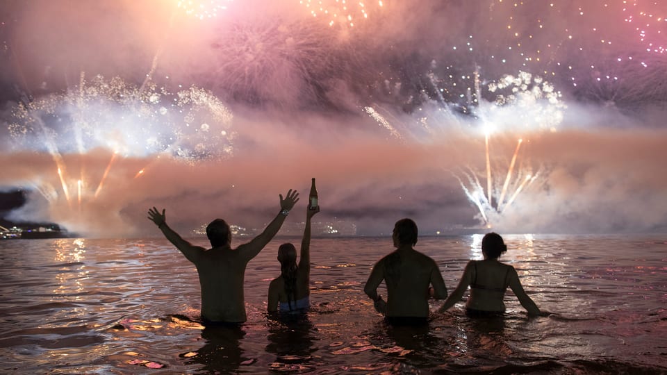 Vier Menschen stehen im Meer, über ihnen Feuerwerk