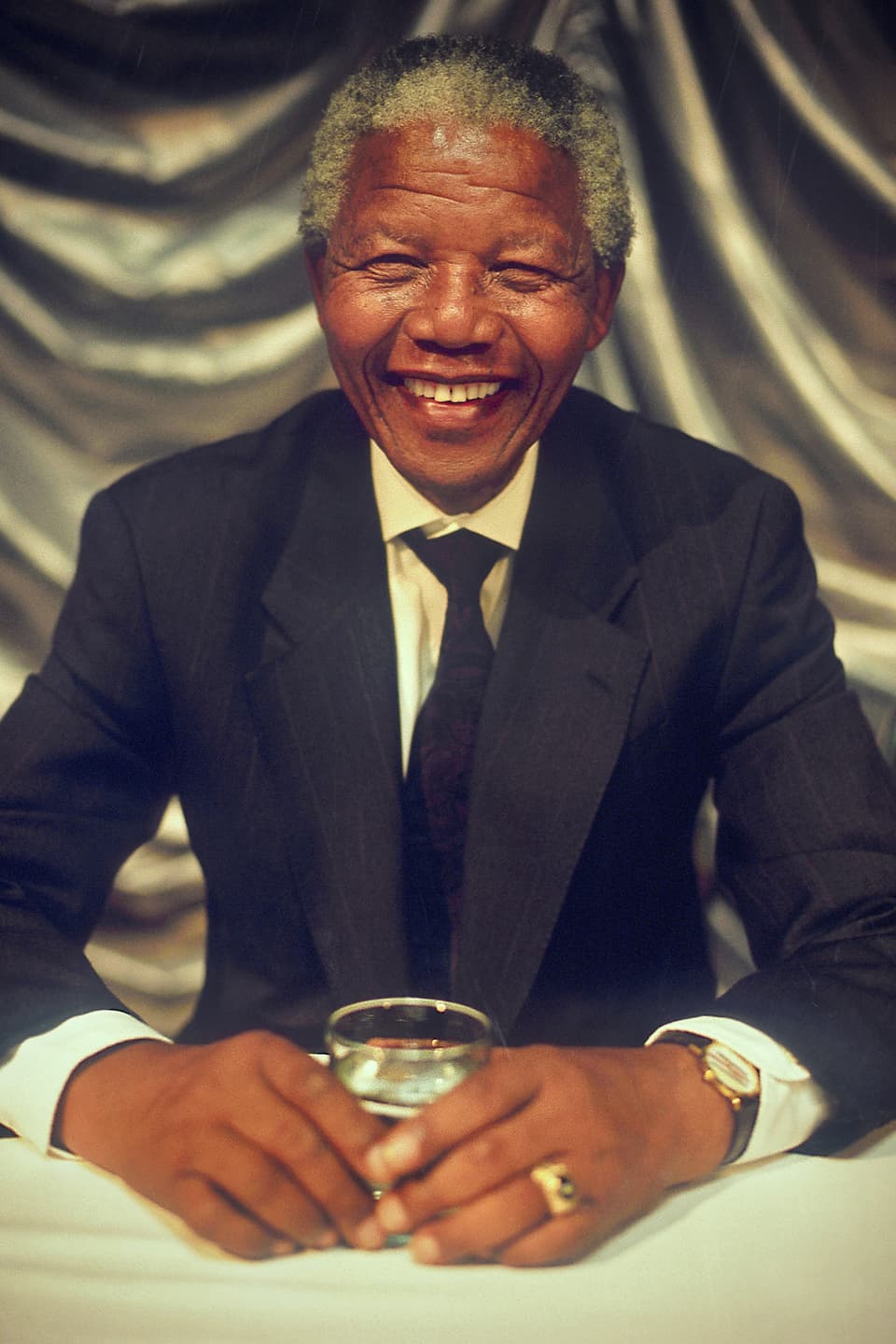 Nelson Mandela lachend und am Tisch sitzend. 