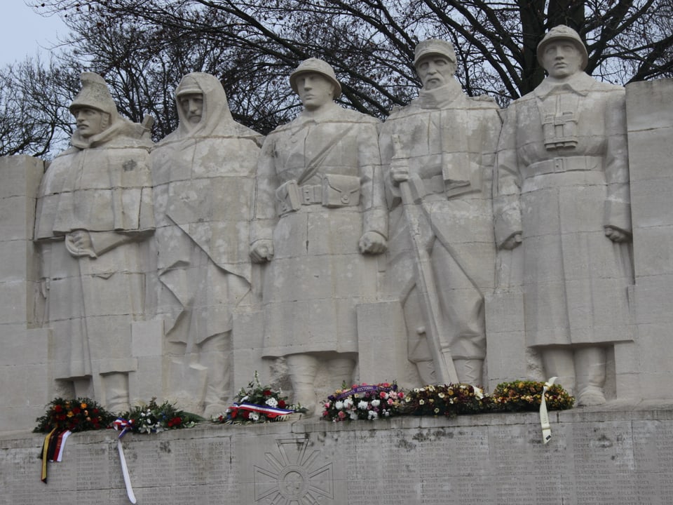 Denkmal mit Statuen von Soldaten. Zu ihren Füssen liegen Blumenkränze.