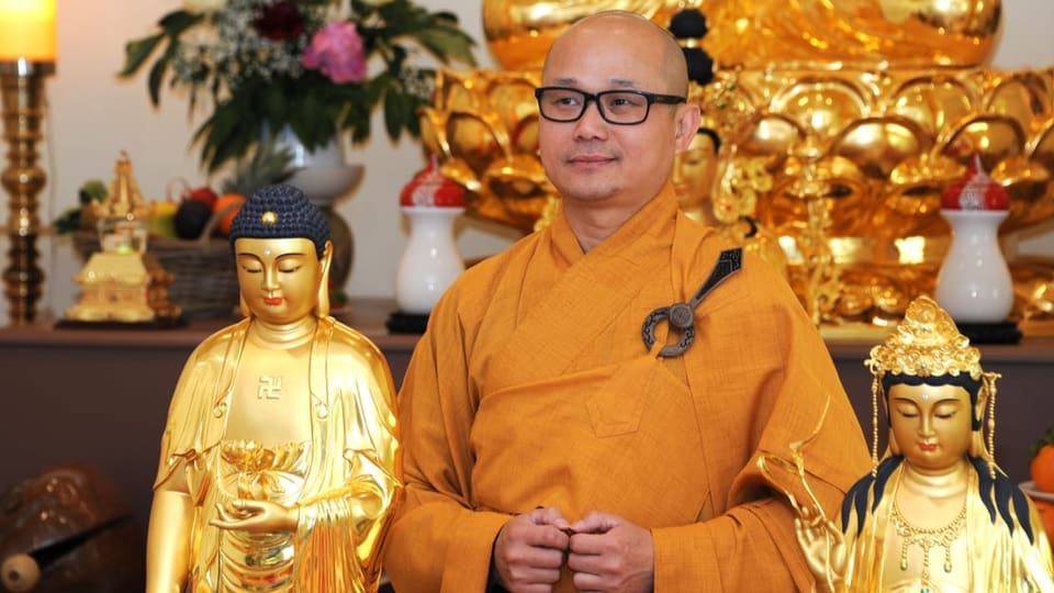 Mann in gelbem Gewand neben den goldenen Buddha-Statuen