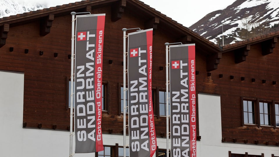 Fahnen des Skigebietes Andermatt-Sedrun flattern vor einem Haus in Andermatt