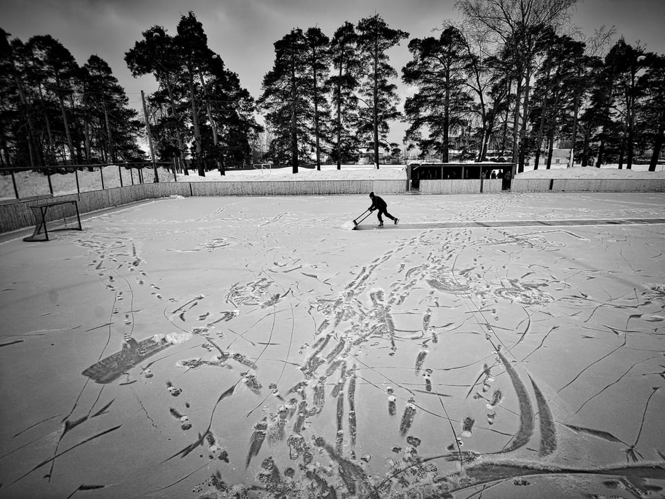 Mann beim Schneeschaufeln auf Eisbahn.