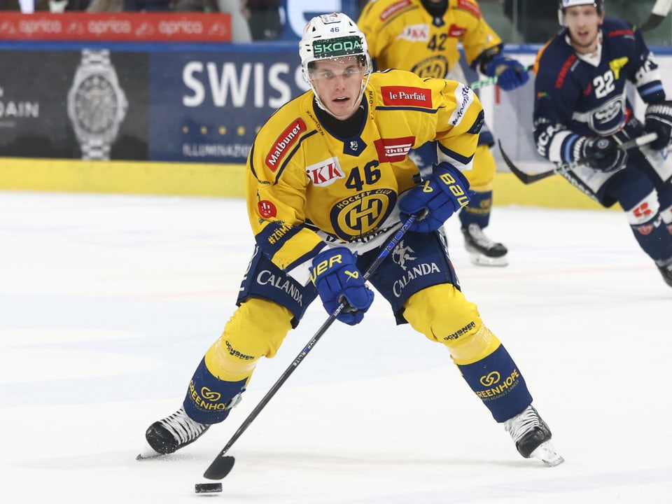 Eishockeyspieler in gelber Ausrüstung spielt Puck auf dem Eis.