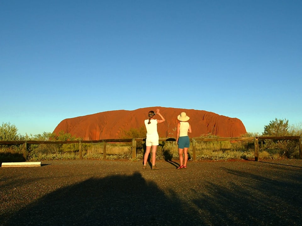 Touristen fotografieren den Uluru von weitem.