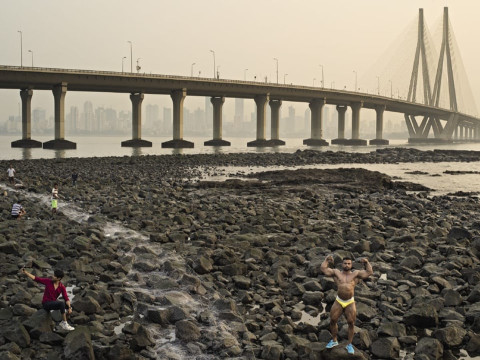 Mann mit muskulösem Oberkörper posiert in Unterhose vor einer grossen Hängebrücke