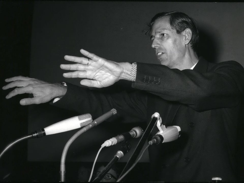 Jacques Piccard auf einem Schwarz-Weiss-Bild. Er steht gestikulierend hinter Mikrofonen.