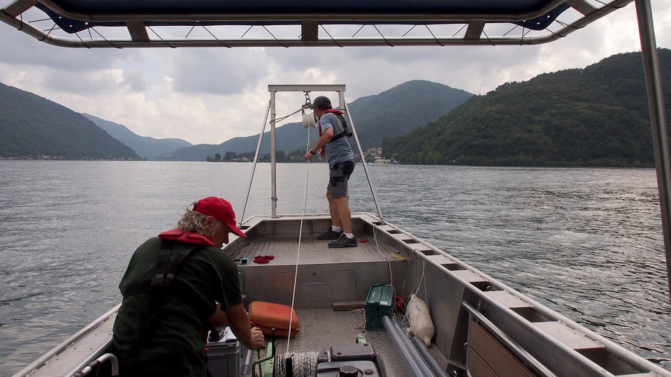 Zwei Männer auf einem Boot. Rechts der Monte San Giorgio.