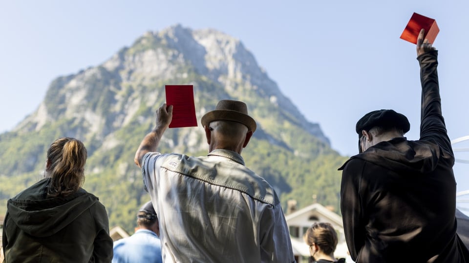 Menschen heben rote Stimmzettel vor einem Berg.