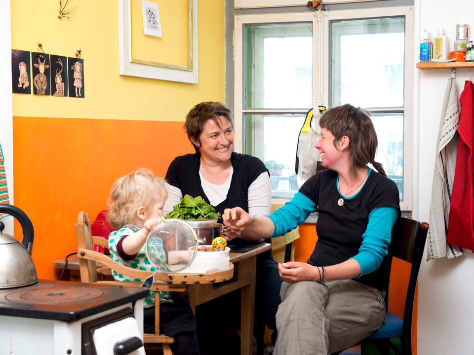 Zwei Frauen an einem Küchentisch, vor ihnen ein Kind.