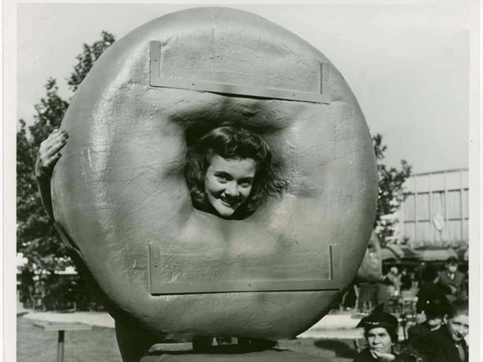 Eine Frau steckt ihren Kopf durch einen überdimensionalen, künstlichen Donut 