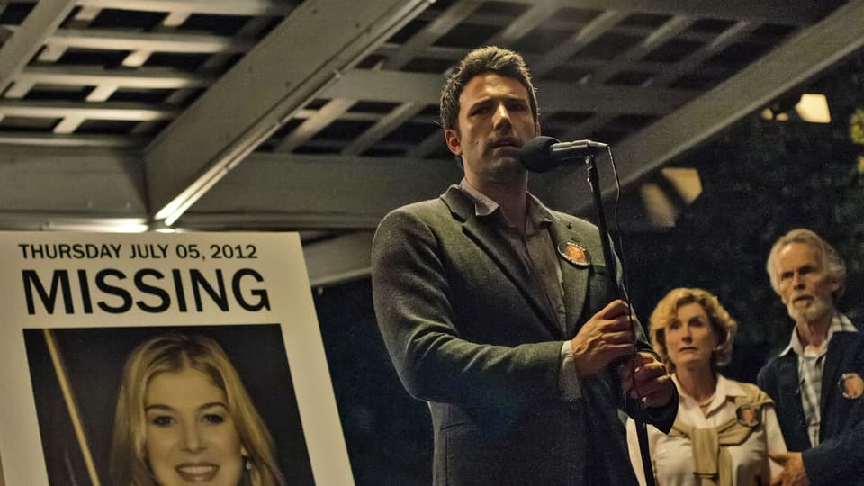 Auf dem Bild ist Ben Affleck als Nick Dunne vor einem Plakat mit seiner vermissten Frau zu sehen.