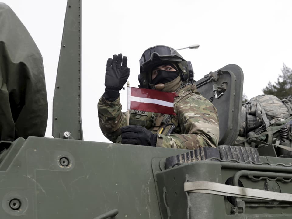 Ein Soldat in einem Panzer hält ein lettisches Fähnlein.
