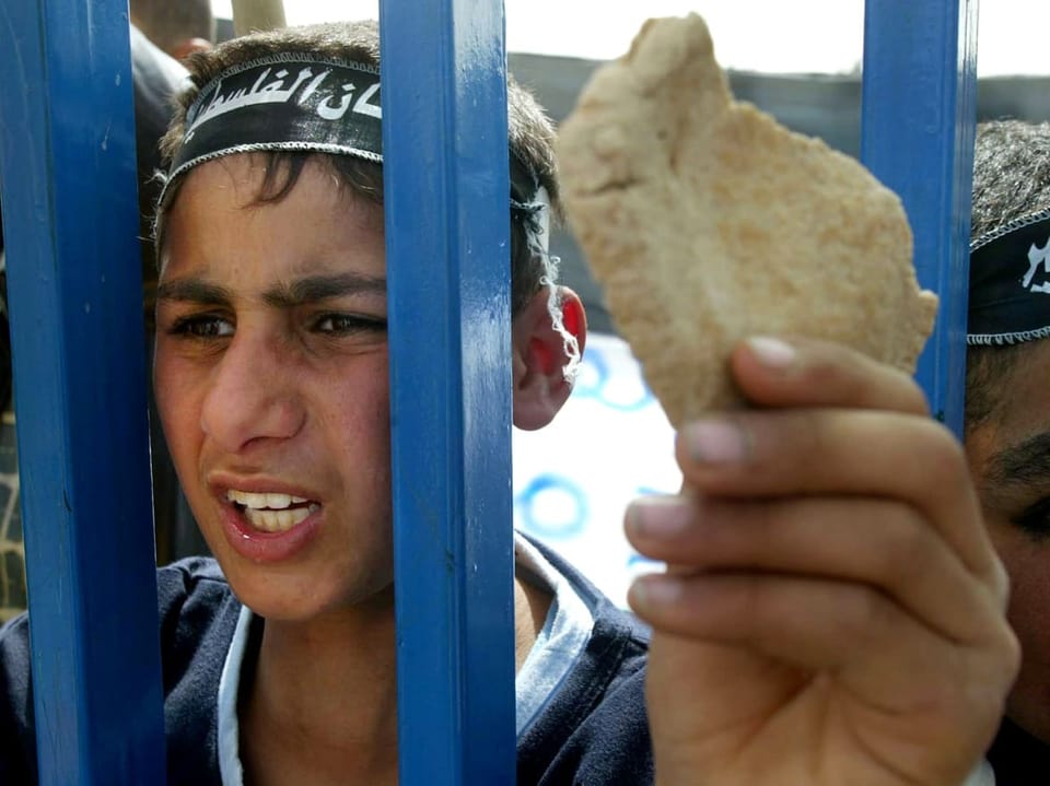 Palästinensischer Junge steht mit einem Stück Brot an einem Zaun.