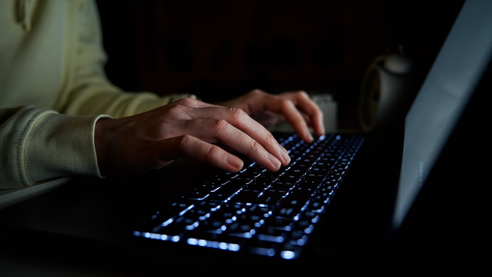 Eine Person bedient im Dunkeln einen Laptop.