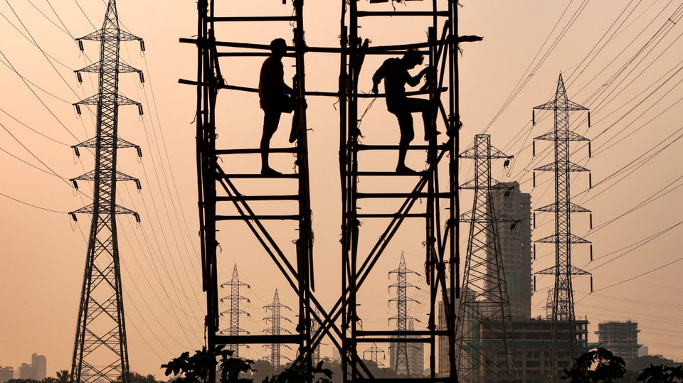 Zwei Männer klettern Strommasten hoch, im Hintergrund ist die Abenddämmerung zu erkennen
