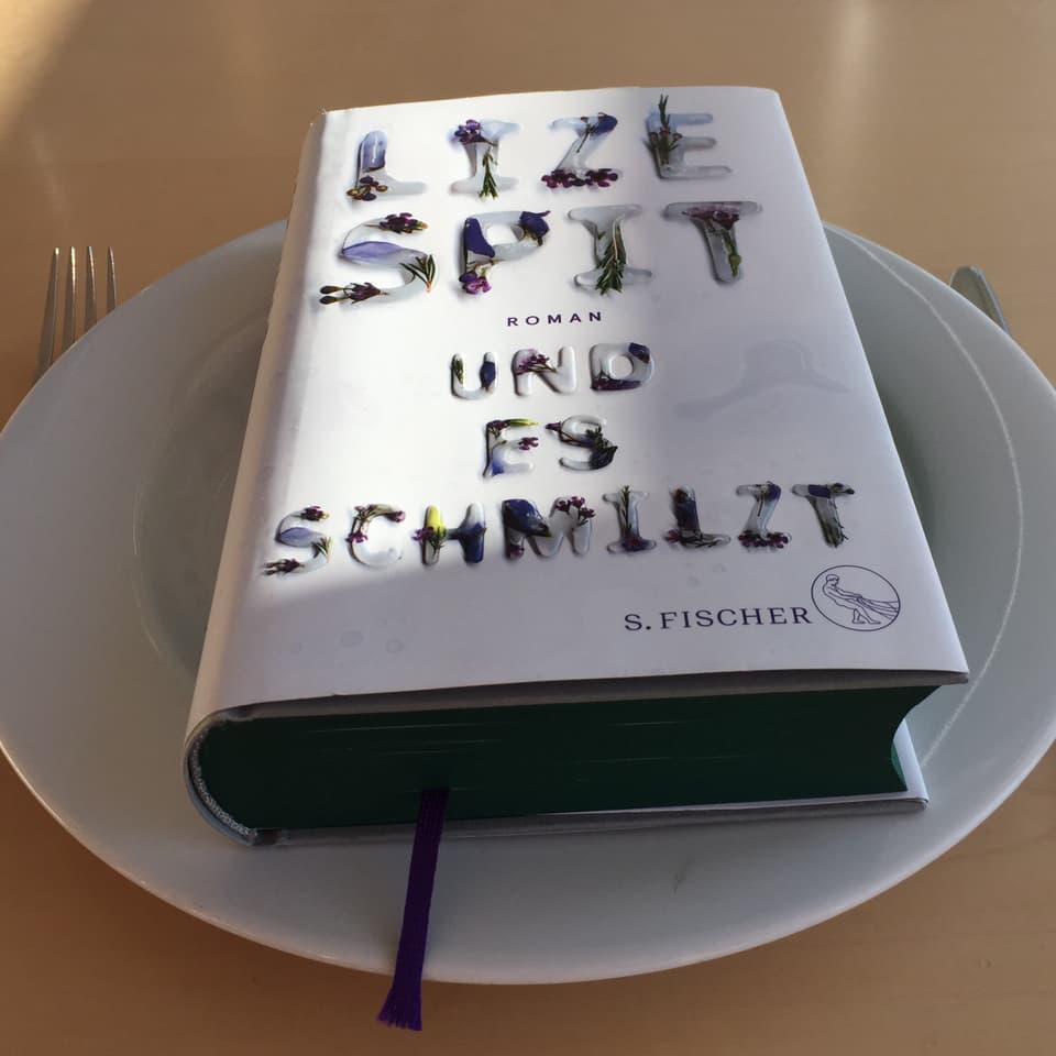 Der Roman «Und es schmilzt» von Lize Spit liegt auf einem weissen Teller. Messer und Gabel daneben.