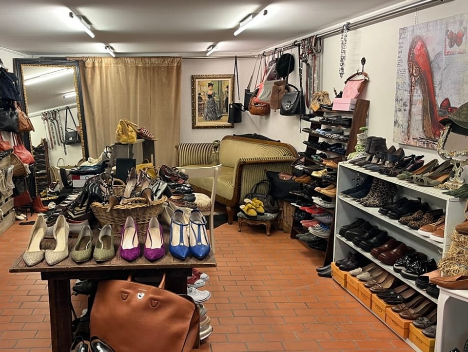 Der Schuhstall von vorne fotografiert. Ganz viele verschieden farbige Schuhe , Schuhbilder an der Wand und ein Sofa.