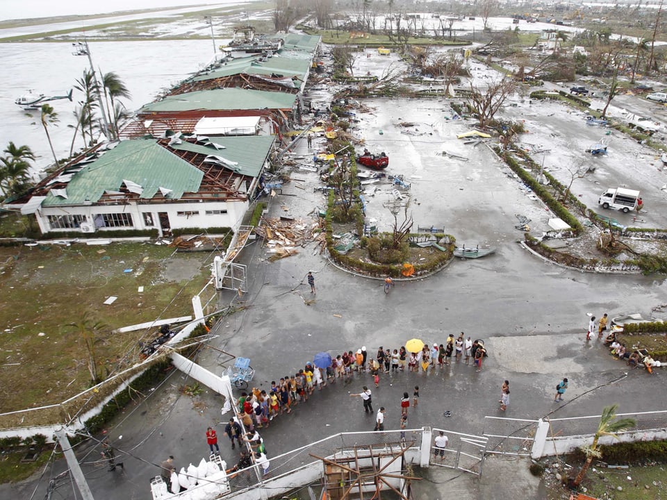 Luftbild des Flughafens Tacloban nach dem verheerenden Sturm: zerstörte Häuser und zahlreiche Menschen, die flüchten wollen. 
