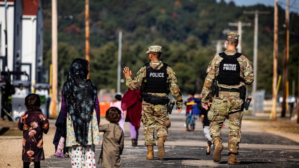 Zwei Militärangehörige gehen an einer Frau mit Kopftuch und zwei kleinen Kindern an der Hand vorbei.