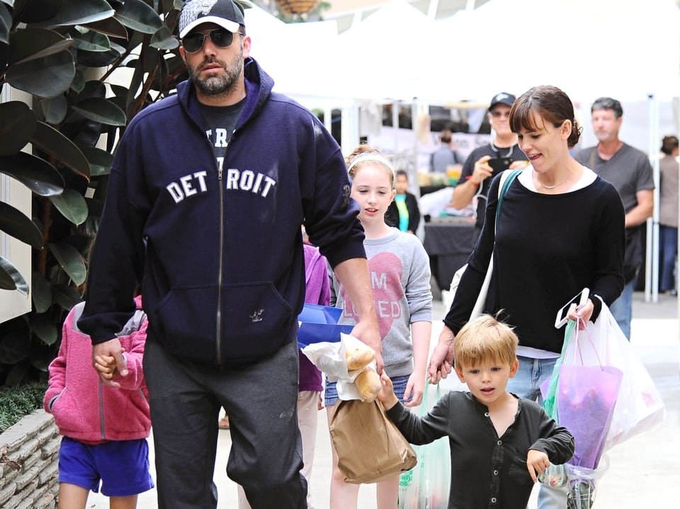 Ben Affleck mit einem Mädchen und einem Jungen an der Hand.  Im Hintergrund geht Jennifer Garner mit Tüten bepackt und ein Mädchen läuft neben ihr her.