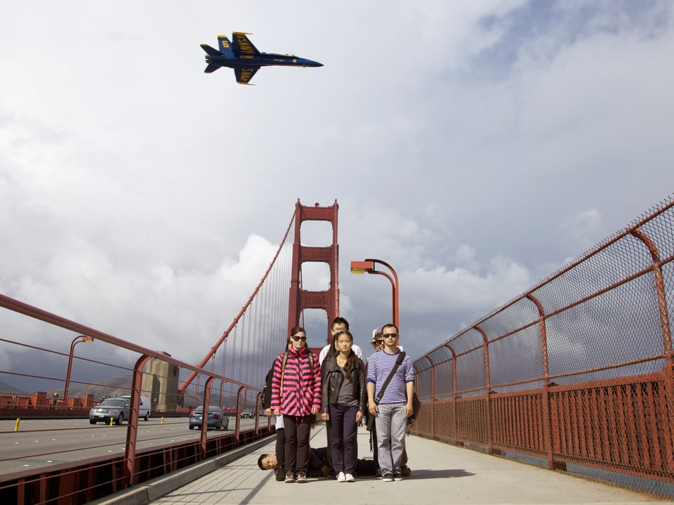 Menschen auf einer Brücke, am Himmel ein Kampfjet.