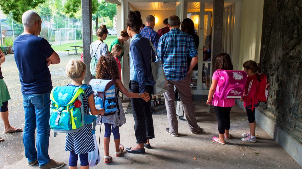 Eltern mit Kindern vor einer Schule am ersten Schultag.