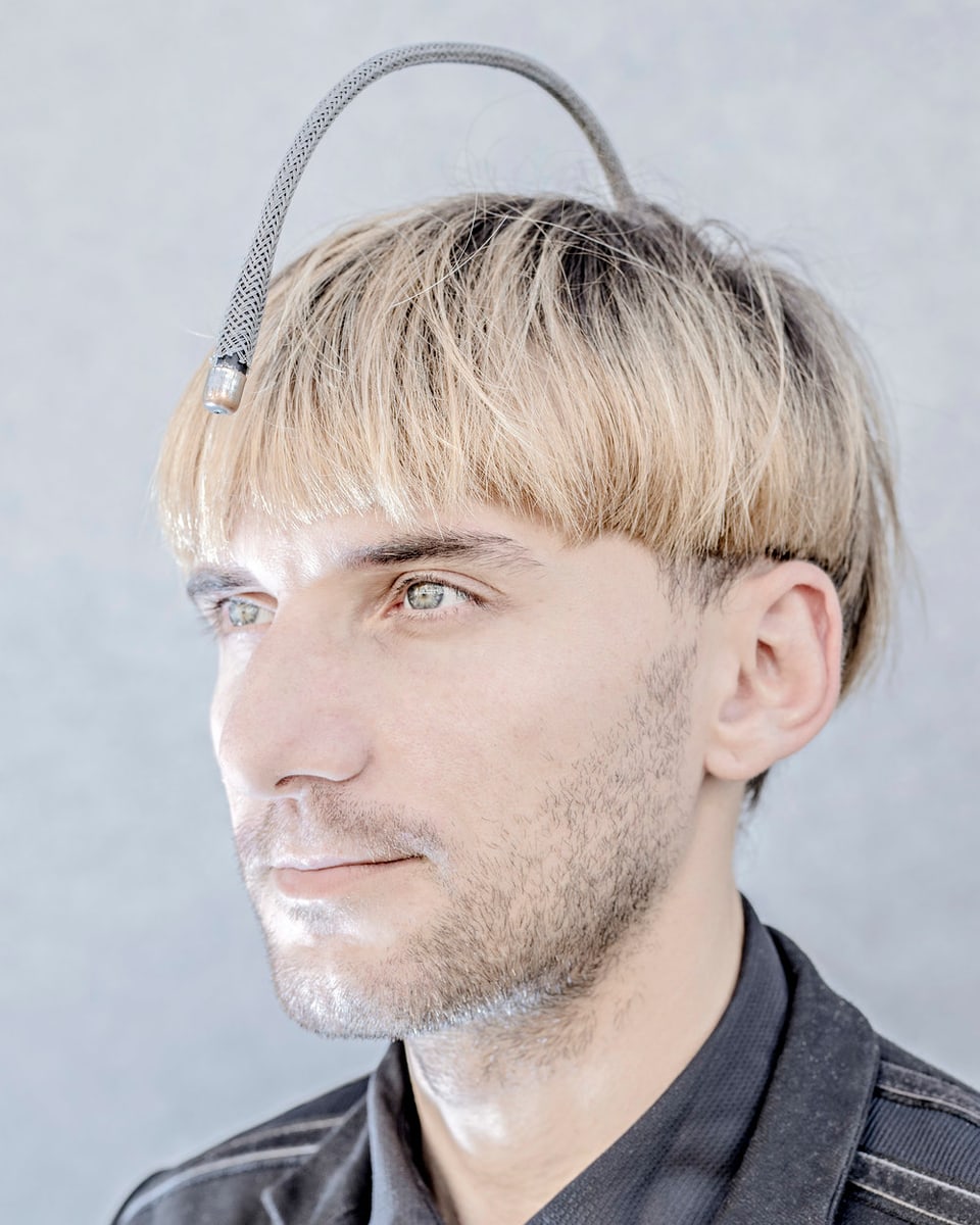 Ein blonder Mann trägt eine gekrümmte Antenne auf dem Kopf.