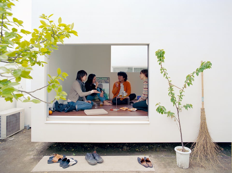 Blick durch ein Fenster: mehrere Leute sitzen gemeinsam am Boden und unterhalten sich. 