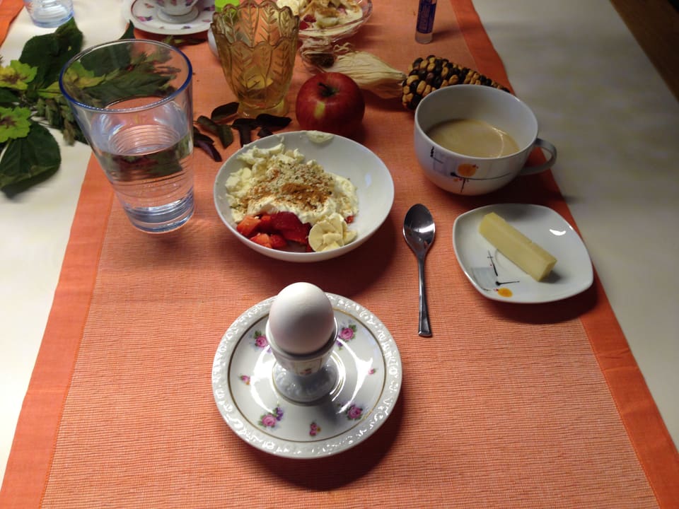 Tisch mit Ei, Stück Käse, Glas Wasser, Müesli.