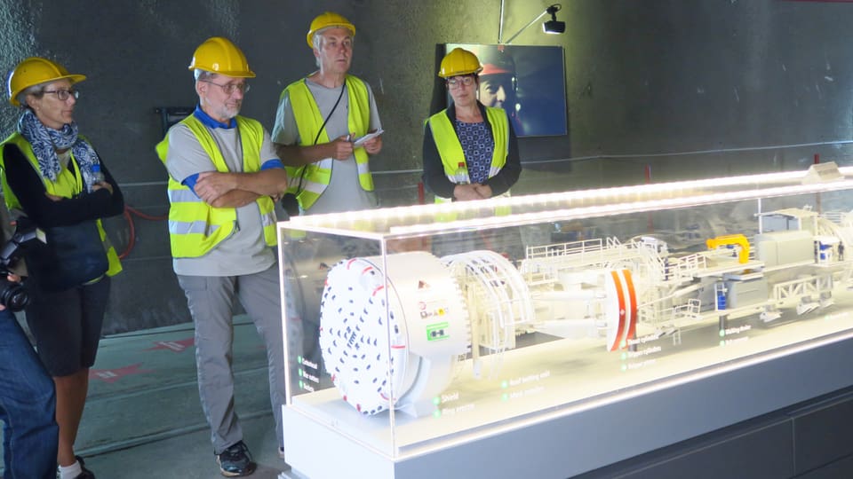 Vier Leute stehen vor einem Glaskasten darin ein Modell einer Tunnelbohrmaschine