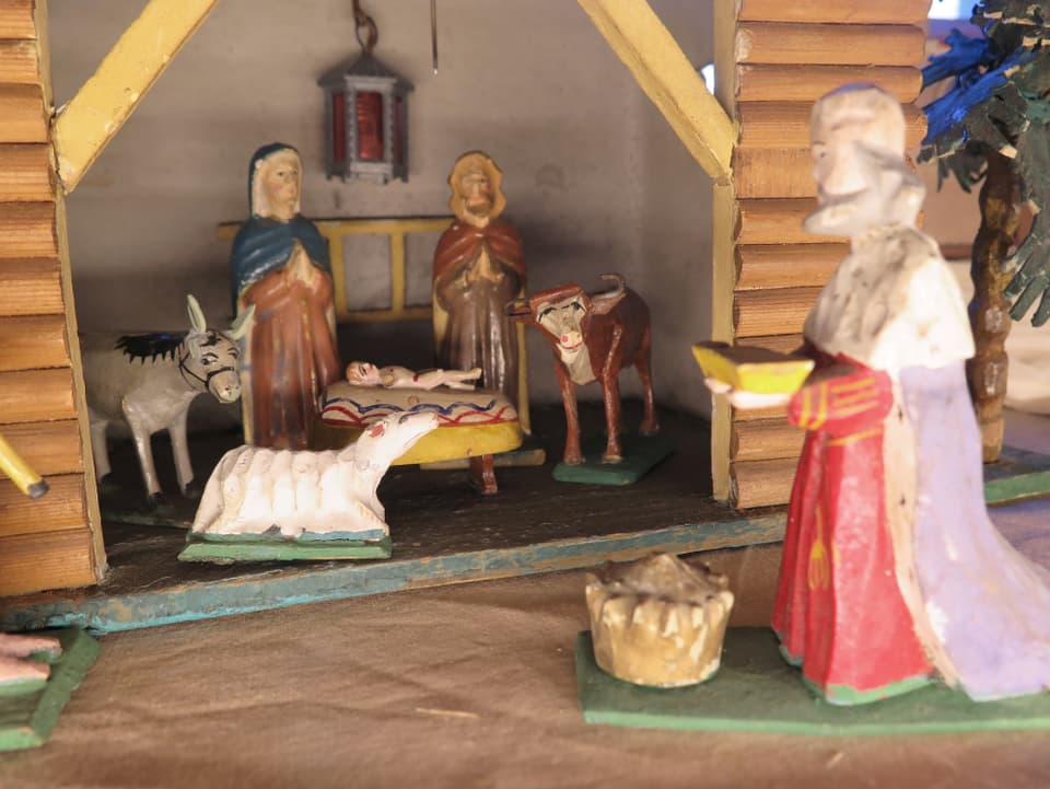 Krippe mit Maria, Joseph und dem Kind in einem Stall, daneben Esel, Schaf und Kuh, ein König bringt ein Geschenk.