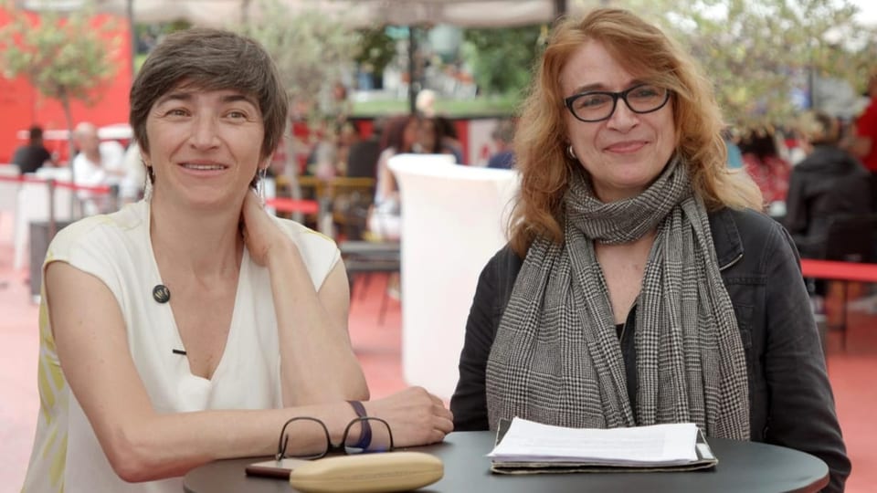 Zwei Frauen sitzen an einem runden Tisch in einem Garten.