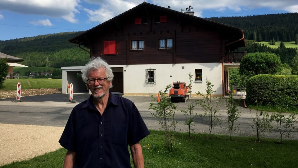 Ein Mann mit grauen Haaren steht vor einem Haus