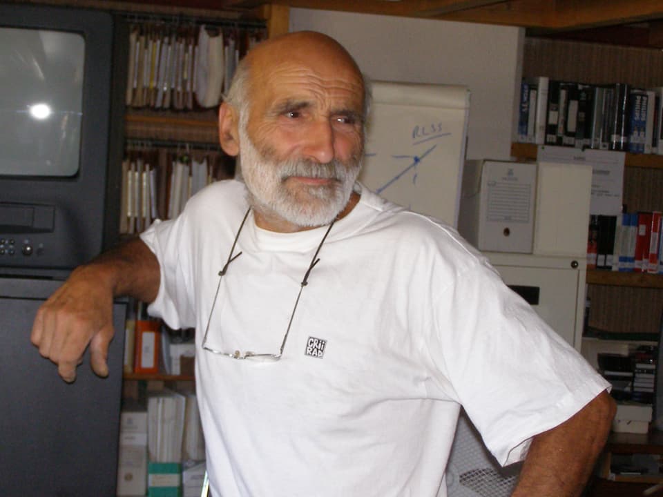 Rolande Desbordes, ein Mann mit weissem Vollbart und weissem T-Shirt, lehnt an einem Schrank.