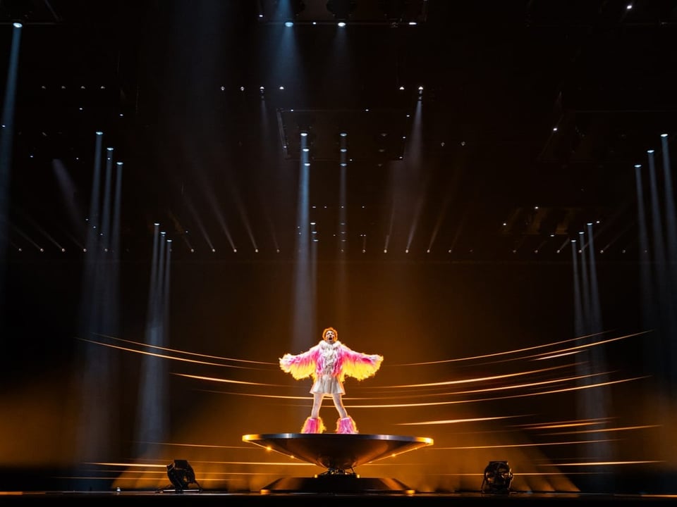 Sänger in farbenfrohem Kostüm auf einer Bühne mit dynamischen Lichteffekten.