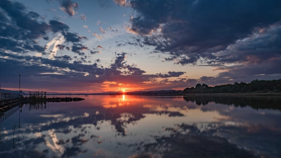 Sonnenaufgang über ruhigem See mit Spiegelung der Wolken im Wasser