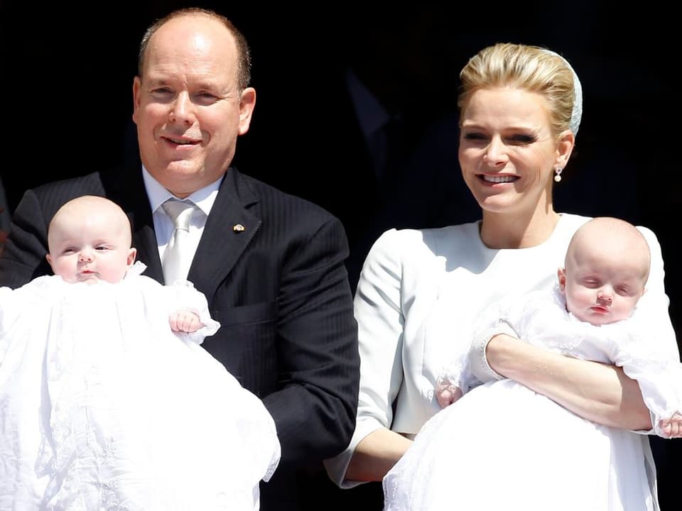 Fürst Albert und Charlène nebeneinanderstehend mit den Babys auf den Armen. 