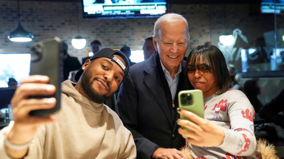 US-Präsident Biden posiert mit zwei Gästen vor deren Handykameras.