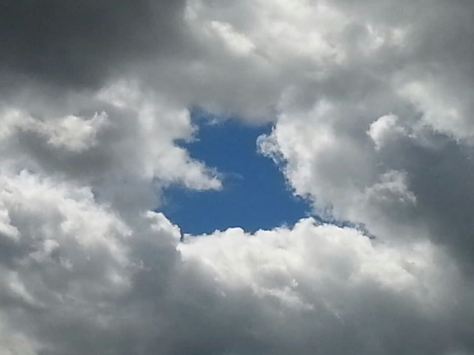 Zum Teil dunkle Wolken am Himmel. Wie ausgestanzt eine Wolkenlücke in Form eines blauen Herzens.