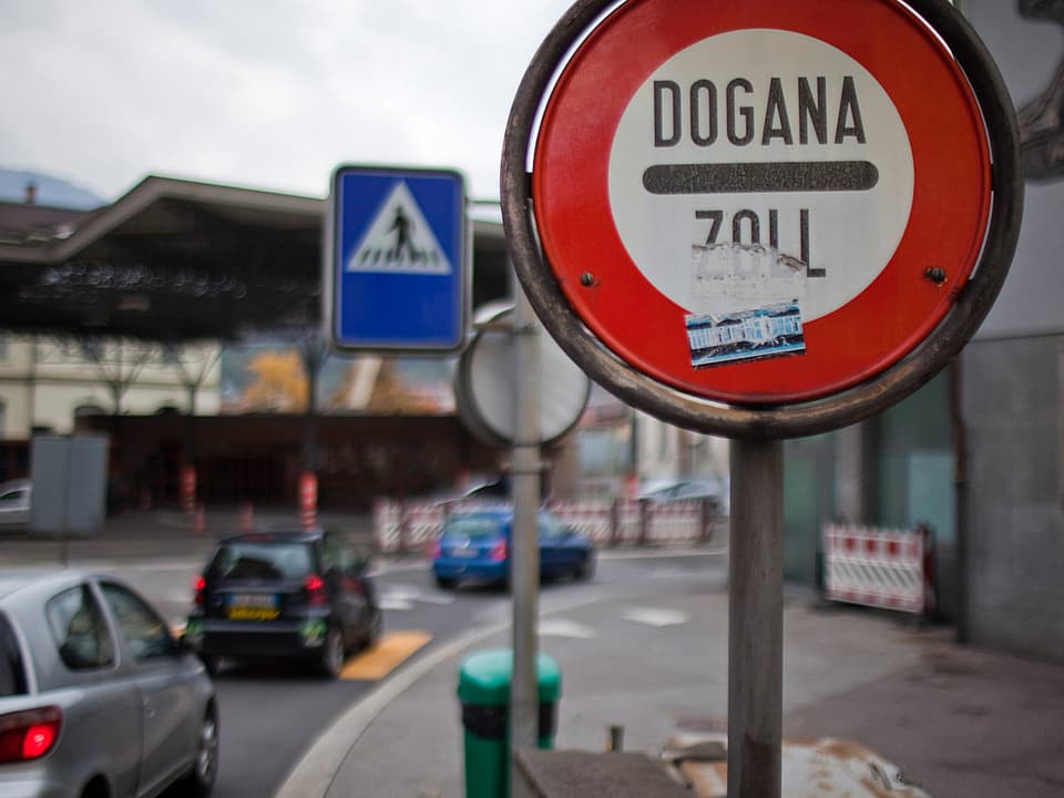 Strassenschild mit der Aufschrift «Dogana/Zoll» im Vordergrund, im Hintergrund Autos beim Zoll.