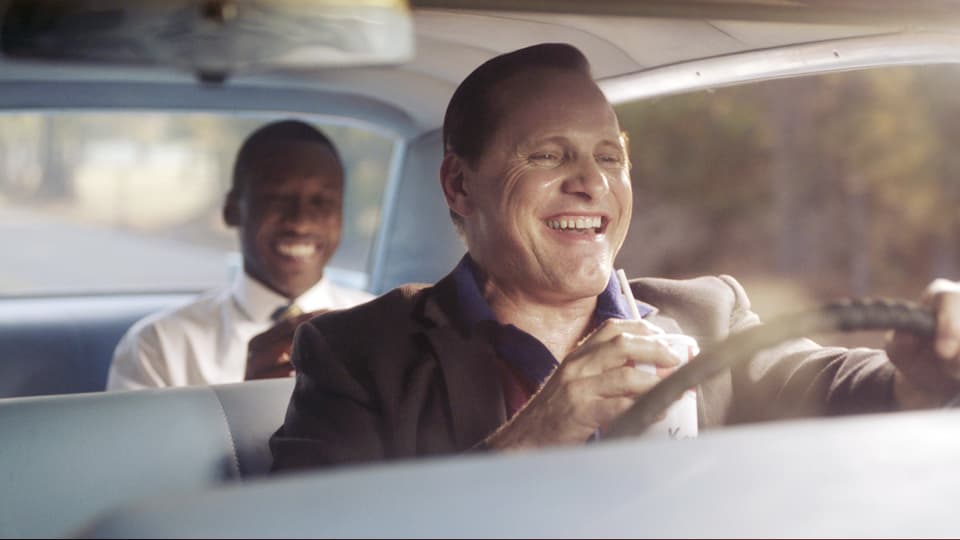 Zwei Männer fahren in den 1950er-Jahren im Auto und lachen zusammen. 