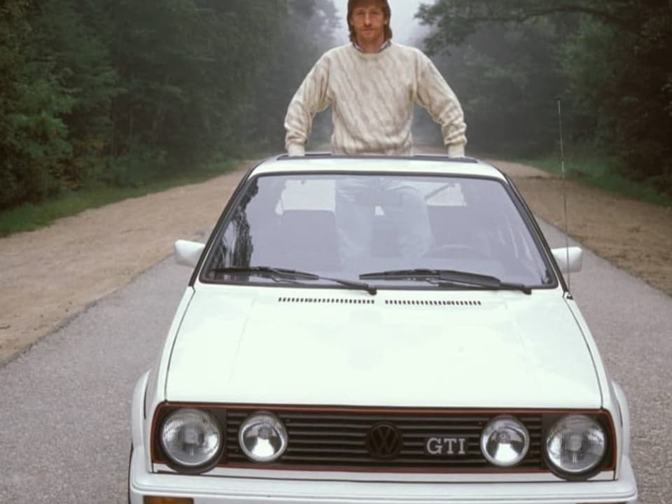 Weisses Cabriolet, Baujahr 80er Jahre. Ein Mann mit zeittypischer Frisur schaut aus dem verdeck heraus.